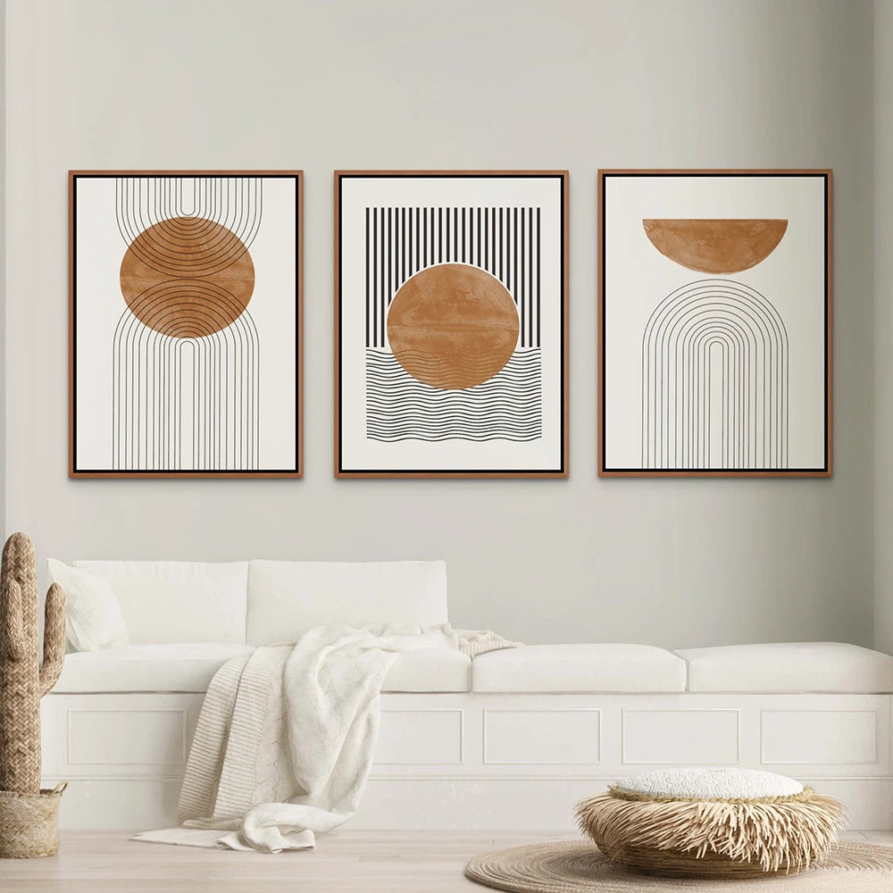 Three abstract art pieces in wooden frames on a wall above a white sofa.