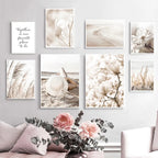 Wall with framed prints of floral and beach scenes, with a vase of flowers on a table.
