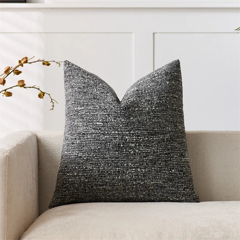 Textured black pillow on a beige sofa with a white wall background