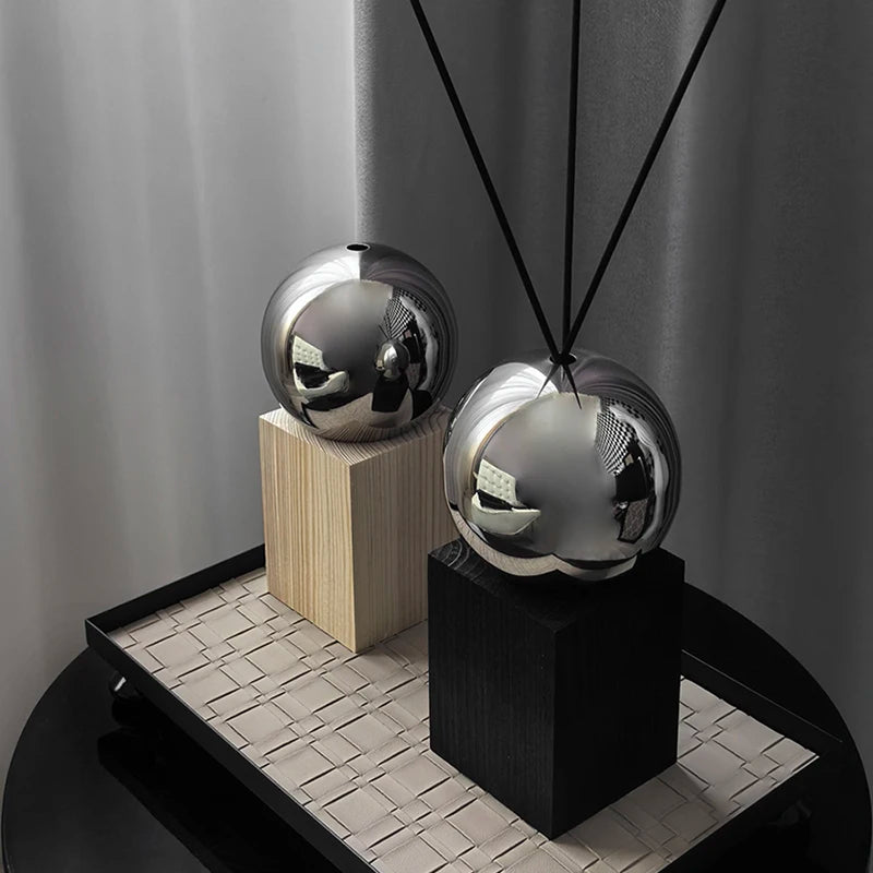 Two metallic spherical objects on wooden and black stands against a neutral background