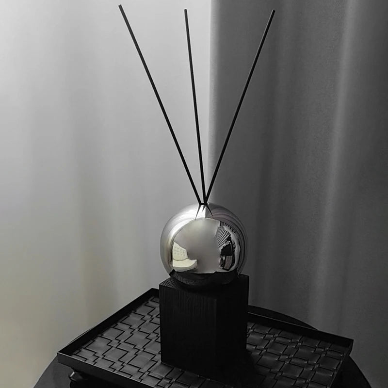 Silver spherical diffuser with black sticks on a textured surface against a plain background