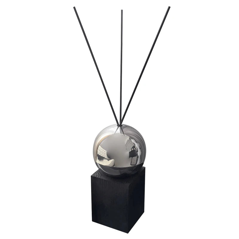 Decorative diffuser with metallic sphere and black sticks on a white background