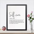 Framed print with 'Self-care' definition on a white wall with decorative items.