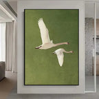 Framed artwork of two swans flying on a green background in a modern interior setting.