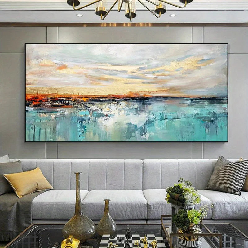 A large abstract canvas painting hanging on a gray paneled wall above a modern light gray sofa in a styled living room. The artwork features a seascape-like composition with turquoise, teal, white, gray, and warm beige tones, plus soft orange and yellow highlights near the horizon.