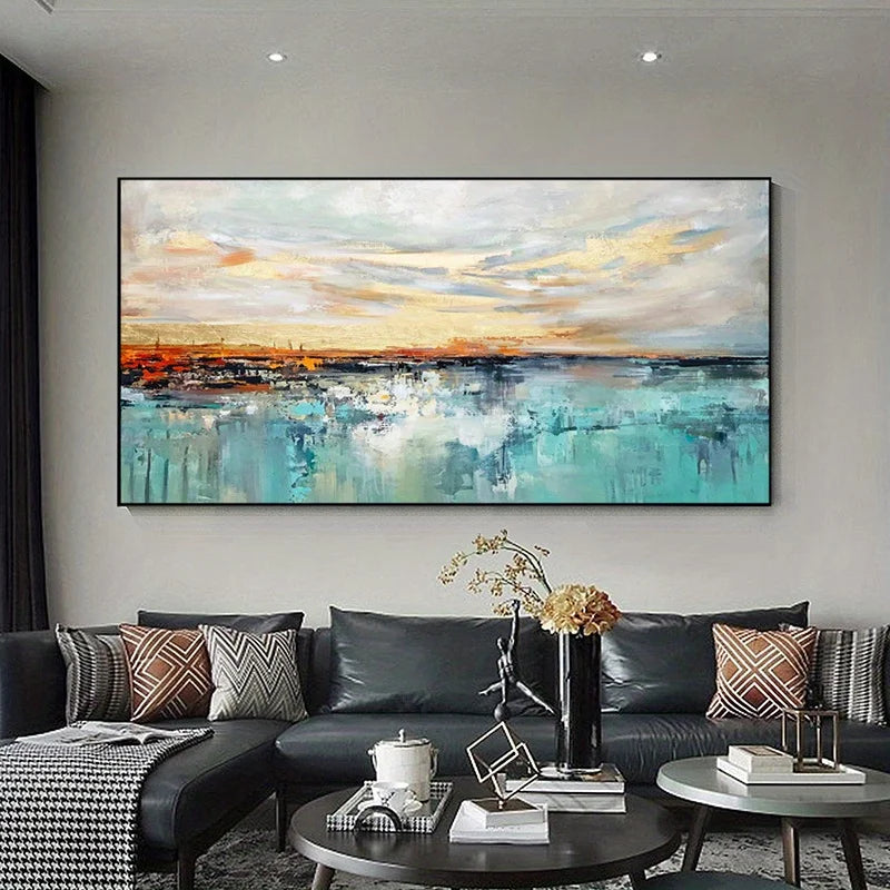 A large abstract landscape painting hangs on a light gray wall above a black leather sectional sofa in a modern living room. The artwork depicts a seascape or sky scene with turquoise water, white and gray clouds, and warm yellow-orange light near the horizon.