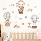 Wall stickers of hot air balloons and stars on a white wall with a wooden crib and teddy bear in the foreground.