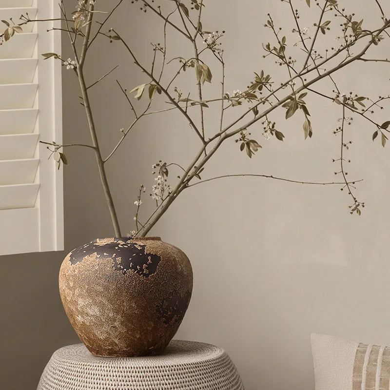 Decorative vase with branches on a textured surface against a neutral wall.