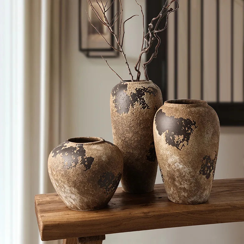 Three rustic ceramic vases on a wooden surface with a neutral background