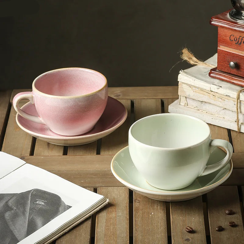 Two ceramic cups and saucers on a wooden surface with a coffee grinder and books in the background.