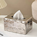 Silver textured tissue box on a white surface with a neutral background