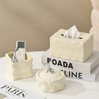 Set of decorative ceramic items including a tissue box, remote control holder, and small bowl on a surface with a beige background.