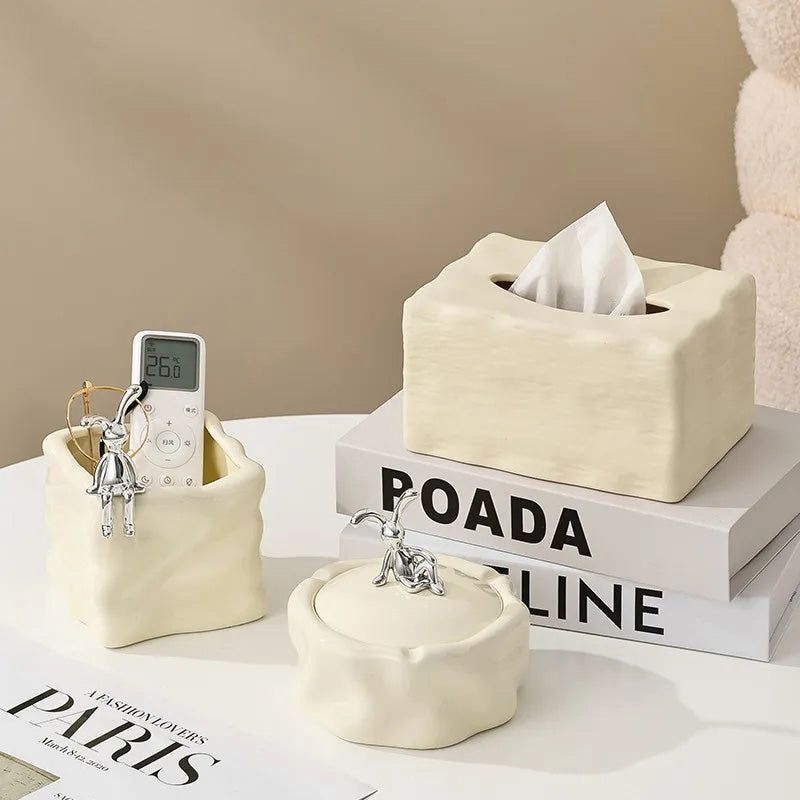 Set of decorative ceramic items including a tissue box, remote control holder, and small bowl on a surface with a beige background.