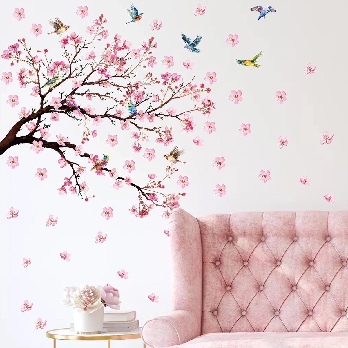 Wall decal of cherry blossom tree with pink flowers and birds on a light gray wall above a pink sofa.