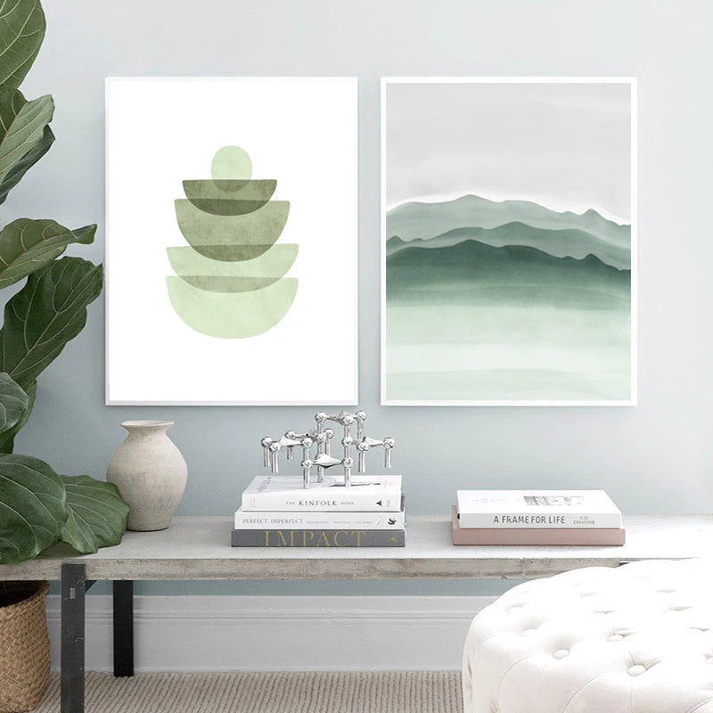 Two framed green abstract artworks on a wall with books and decor items below.