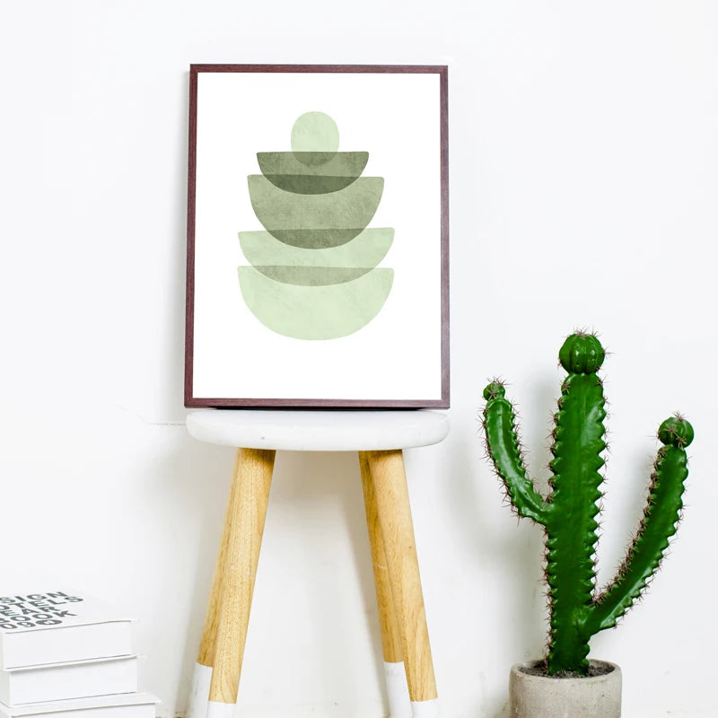 Framed green abstract art on a white wall with a cactus plant below.