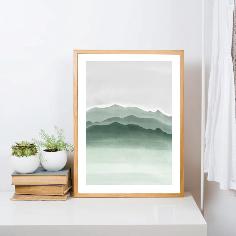 Framed artwork of a mountain landscape on a white surface with books and plants.