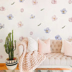 Light pink sofa with decorative pillows and a cactus plant against a floral wallpapered wall.