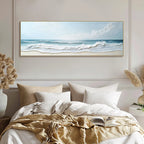 Framed beach scene painting above a bed with beige and white bedding.