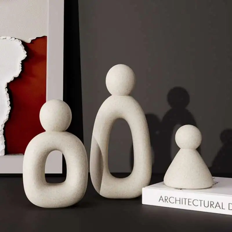 Three white abstract sculptures on a dark surface with a blurred background